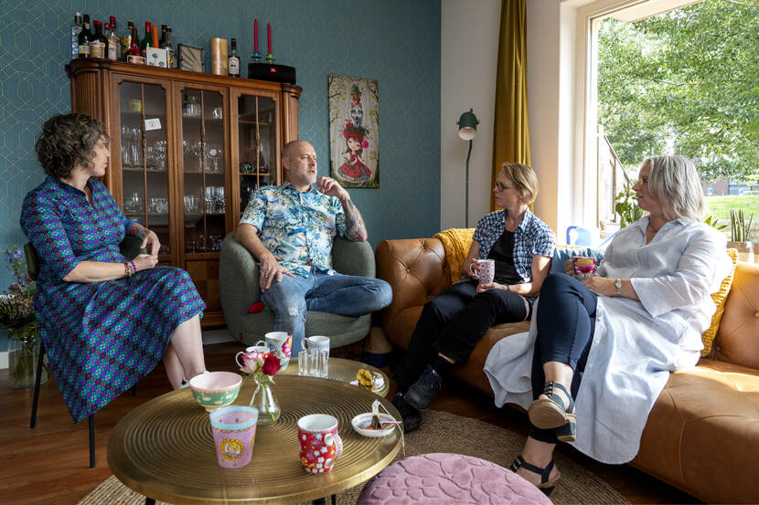 vier mensen zitten in een huiskamer, drinken thee en praten